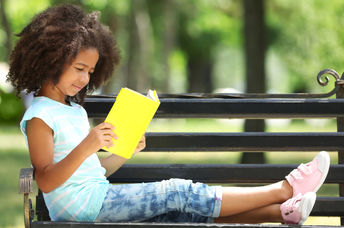 一个年轻的女孩喜欢在公园长凳上读书。