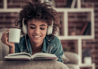 耳机的美国黑人的女孩正在听音乐，读书，喝咖啡