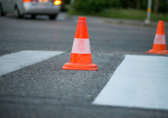 道路交通锥的宏观镜头，橙色和白色条纹站在公路建设工程期间灰色沥青上的街道上。刚刚在人行道上画了白色的街道线