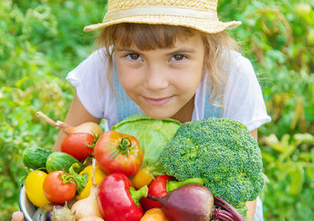 田里的一个小女孩手里拿着一个篮子，里面装满了刚摘下的蔬菜。