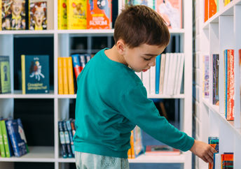 一个八岁的男孩添加自己的书去图书馆的书架。