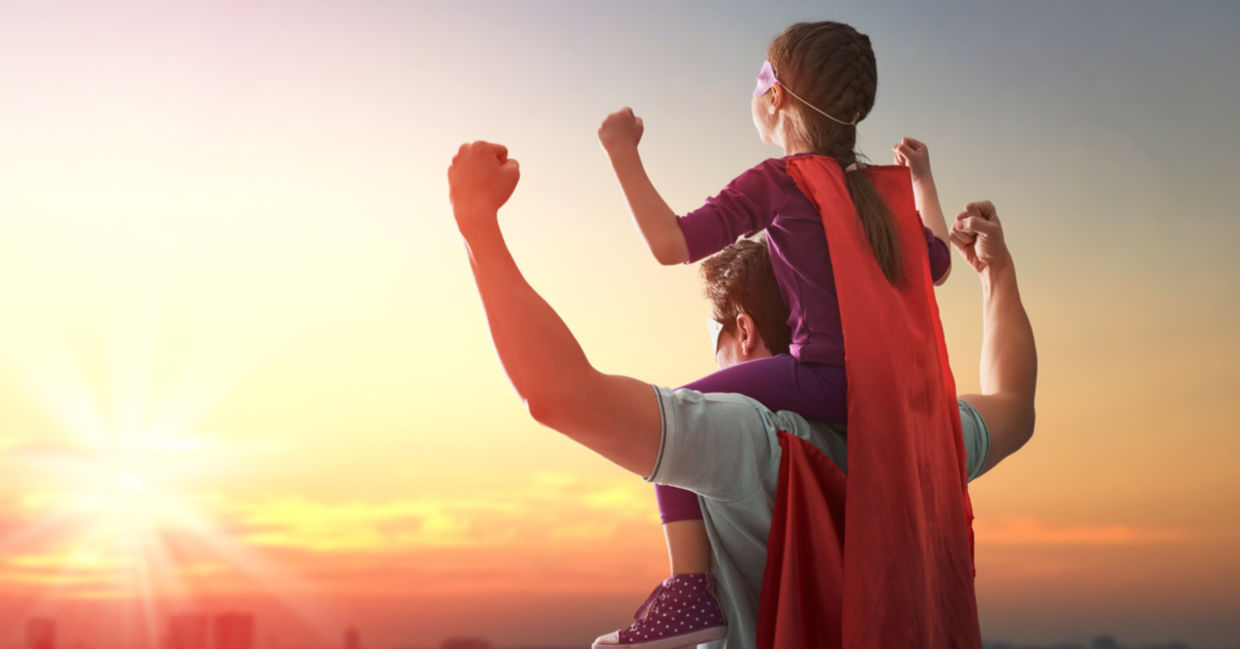 一位父亲把女儿扛在肩上，两人都穿着超级英雄斗篷。