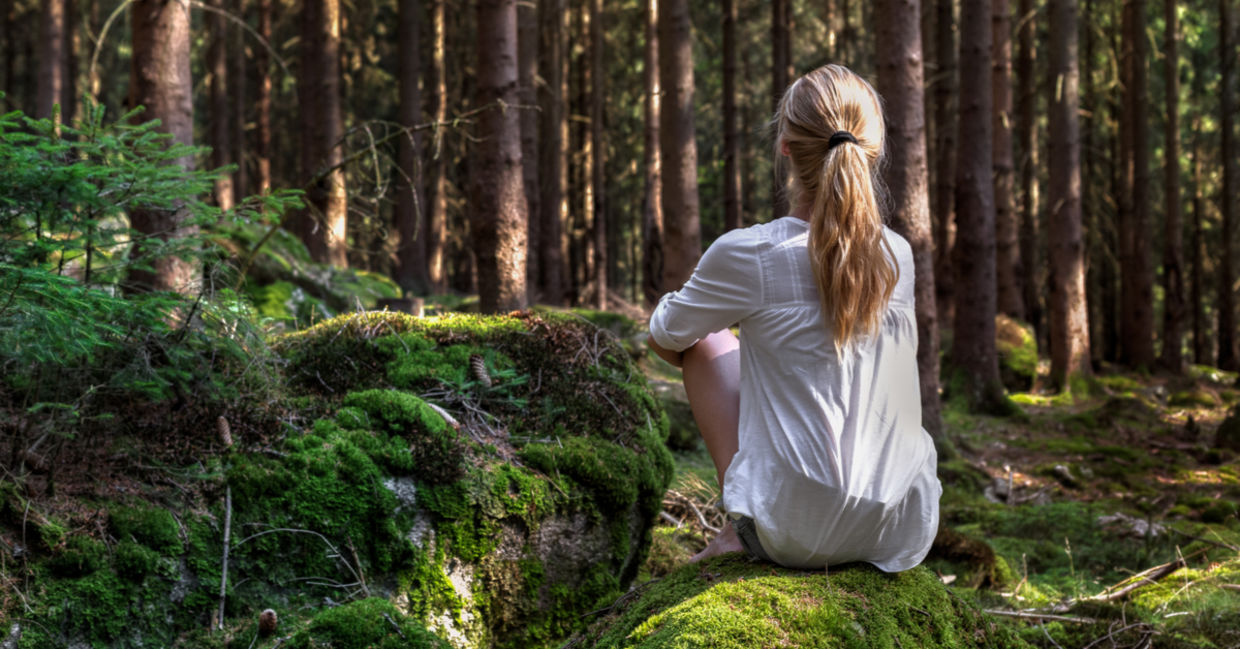 一个女人坐在森林里孤立孤独的苔藓覆盖的岩石。