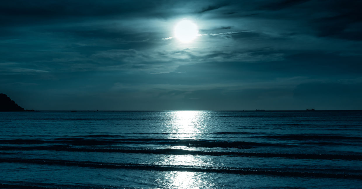 一个满月横跨海面闪耀，在看起来像路的水上产生反射。