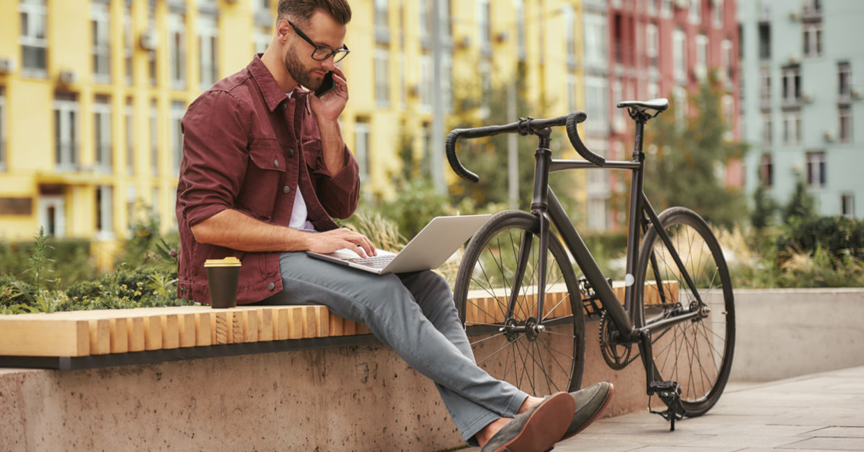 年轻人在笔记本电脑上工作，并在骑自行车附近的长凳上通过电话交谈