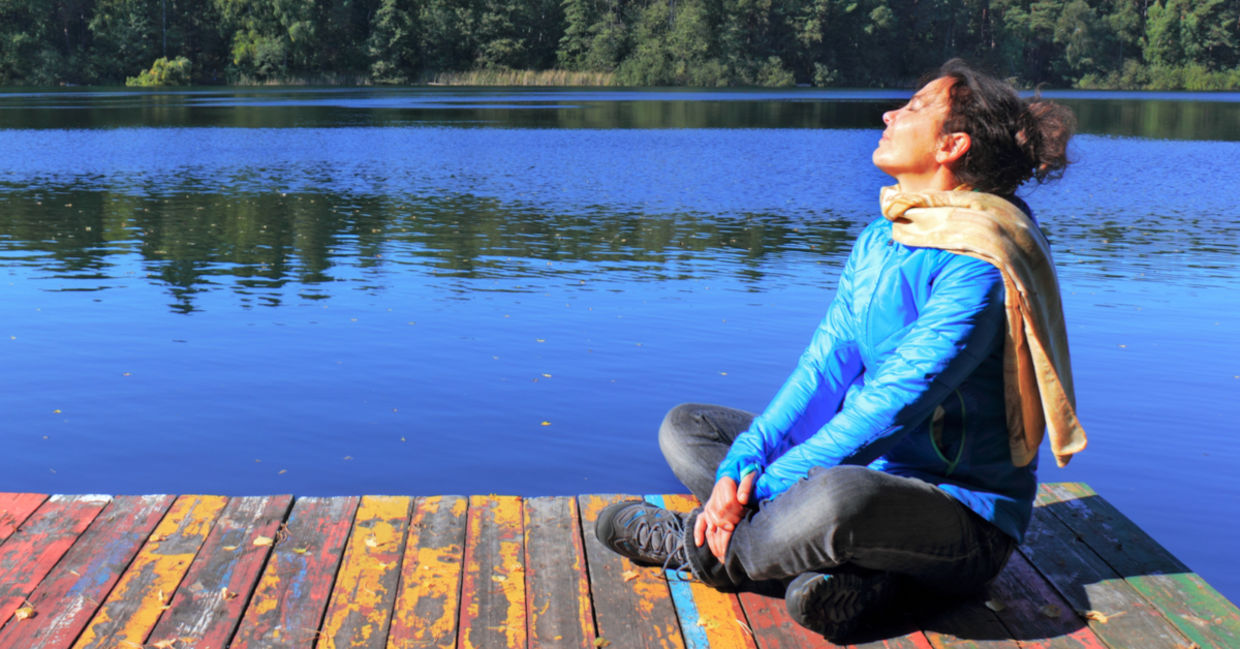 一个女人坐在码头的湖是做呼吸练习来帮助她语气迷走神经。