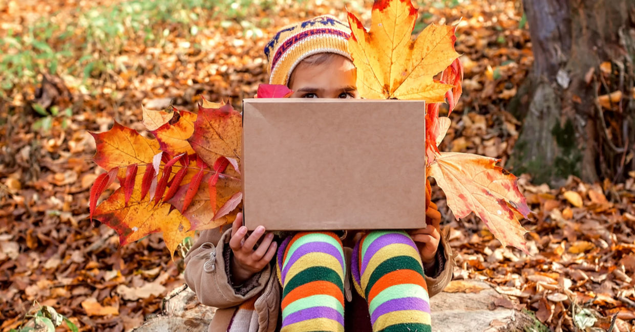 一个抱着秋天的年轻女孩从一个大礼品盒后面​​偷看。