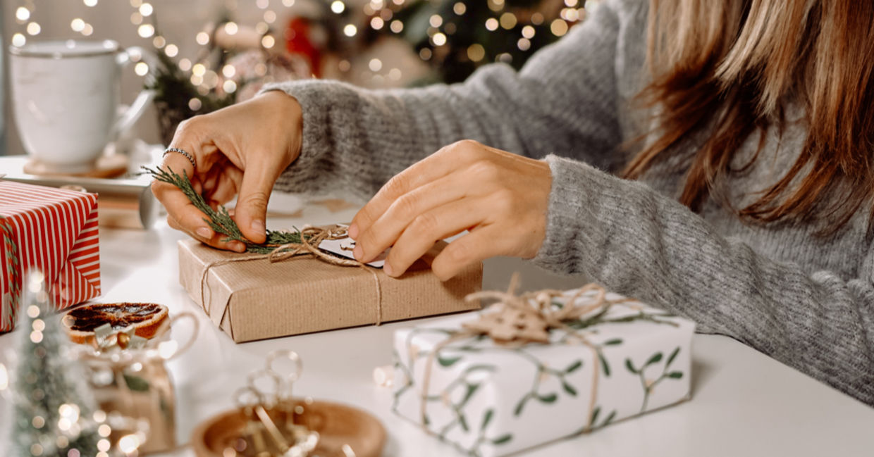 一个女人坐在圣诞节前，用杜松和DIY弓形的小树枝装饰她的礼物。