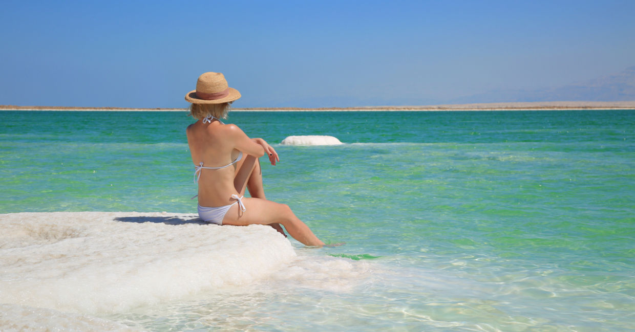 一个女人坐在以色列的死海的盐包装岸上。