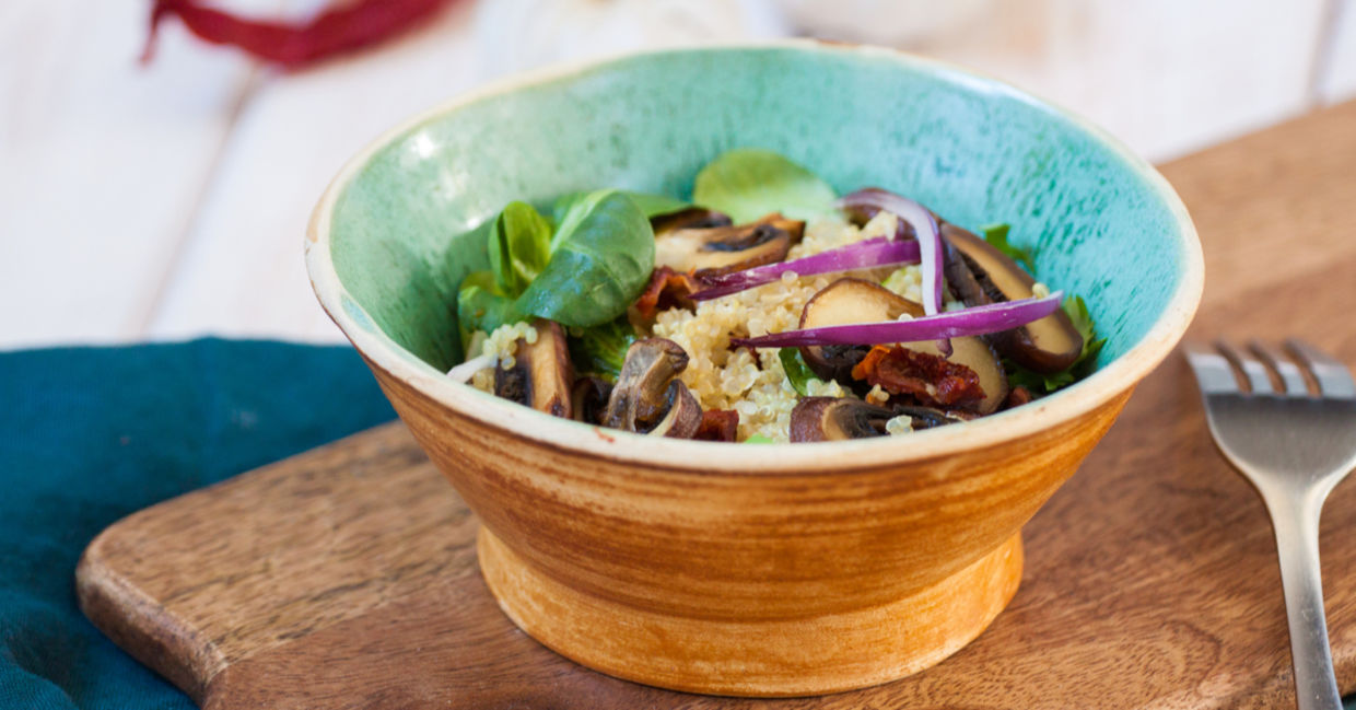 蓝色碗充满新鲜的自创沙拉用奎奴亚藜，菠菜和蘑菇。