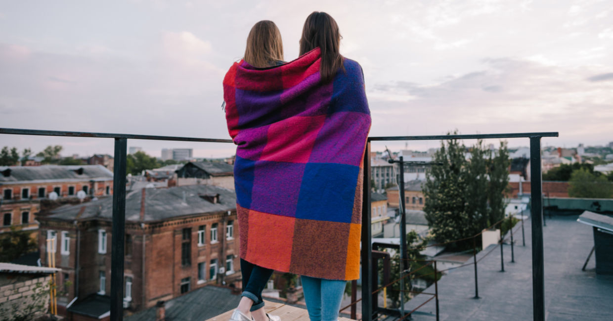 两个朋友包裹在毯子站立在阳台外面。